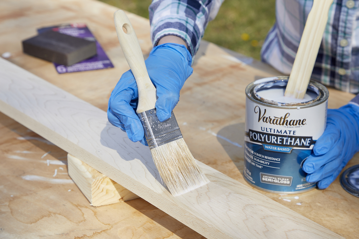 Woman applies polyurethane to wood board with a paint brush.
