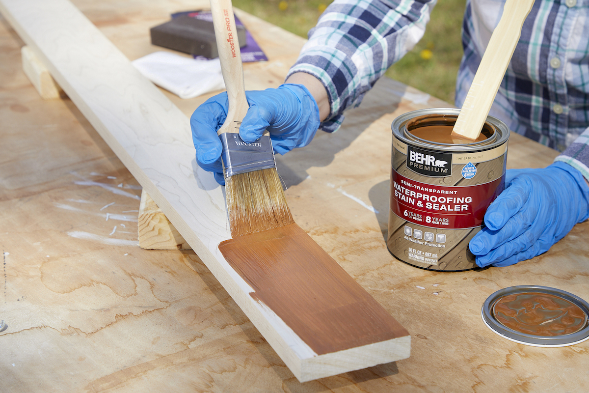 Woman applies brown stain and sealer to waterproof a wood board.