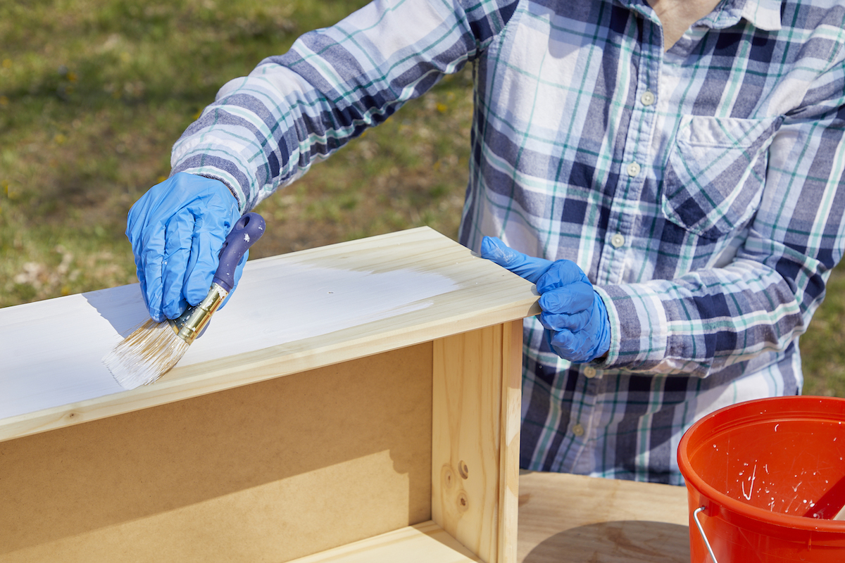 Woman paints a natural wood drawer with whitewash paint.