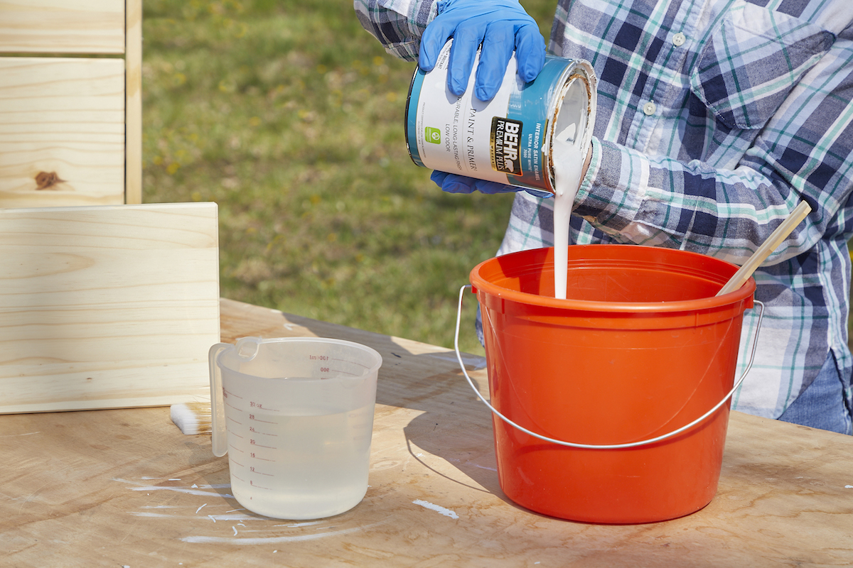 Woman mixes water-based white paint and water in an orange bucket.