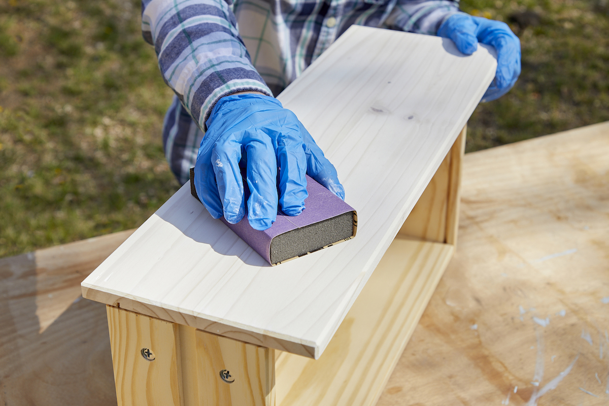Woman uses a sanding block to sand a whitewashed dresser drawer.