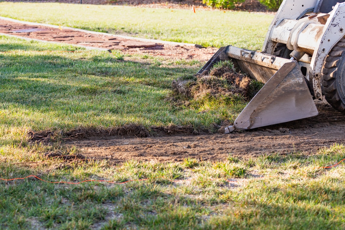 A bulldozer removing a residential lawn to replace it with xeriscape landscaping.