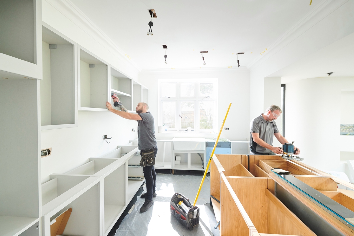 Two professionals are installing an entire kitchen cabinet set.