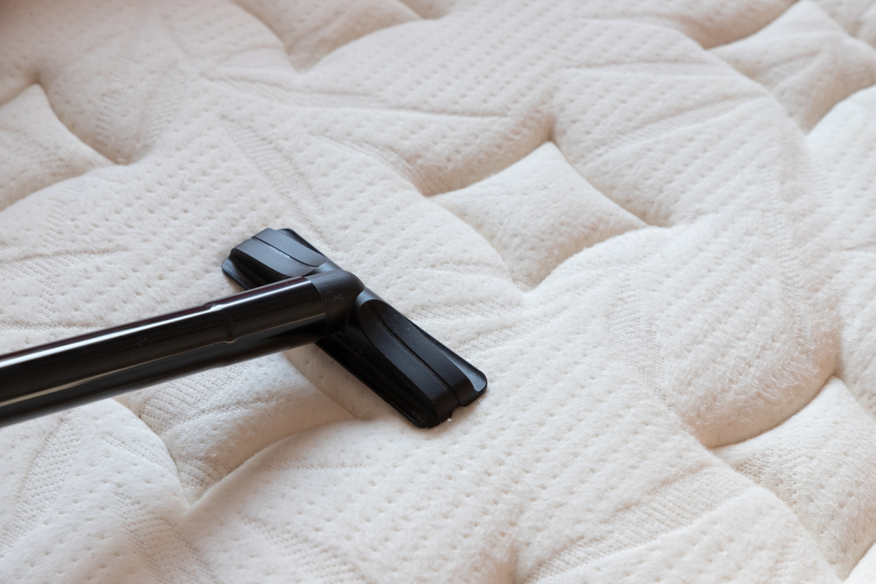 A vacuum cleaning attachment is being run along the surface of an uncovered mattress.