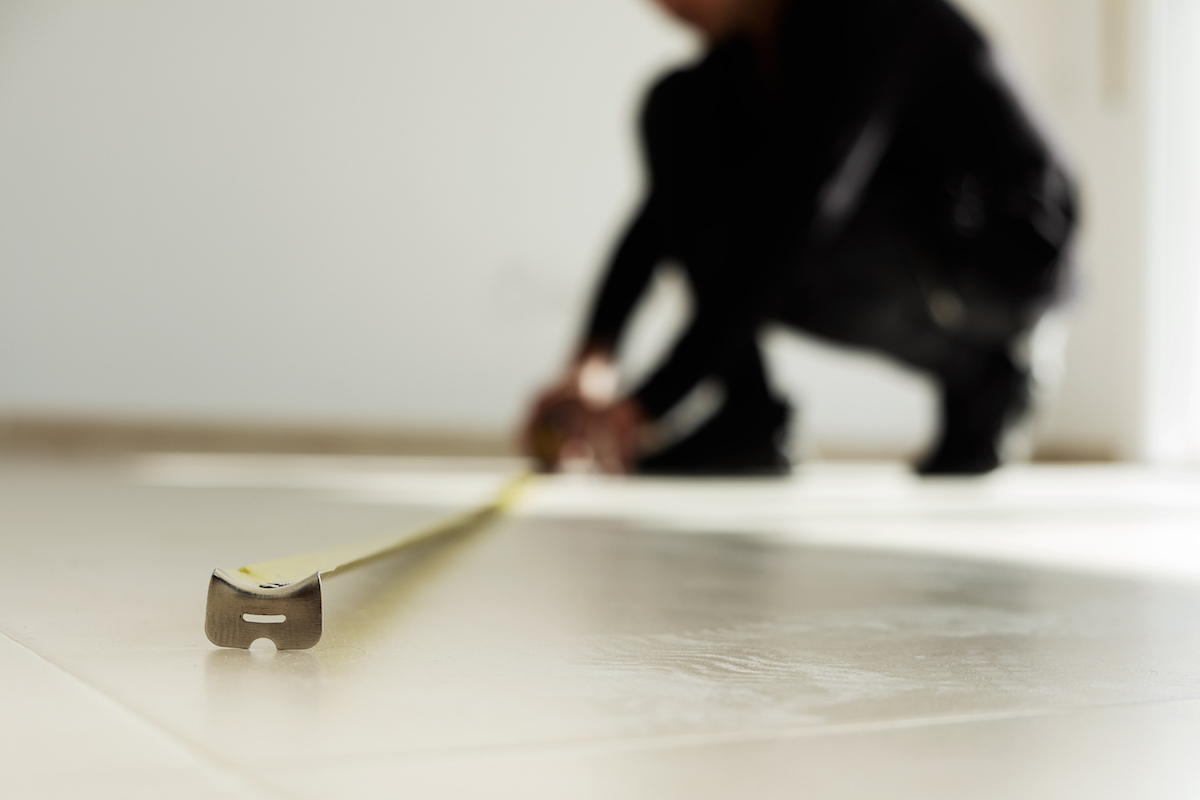 A person is using a measuring tape to measure a tiled floor.