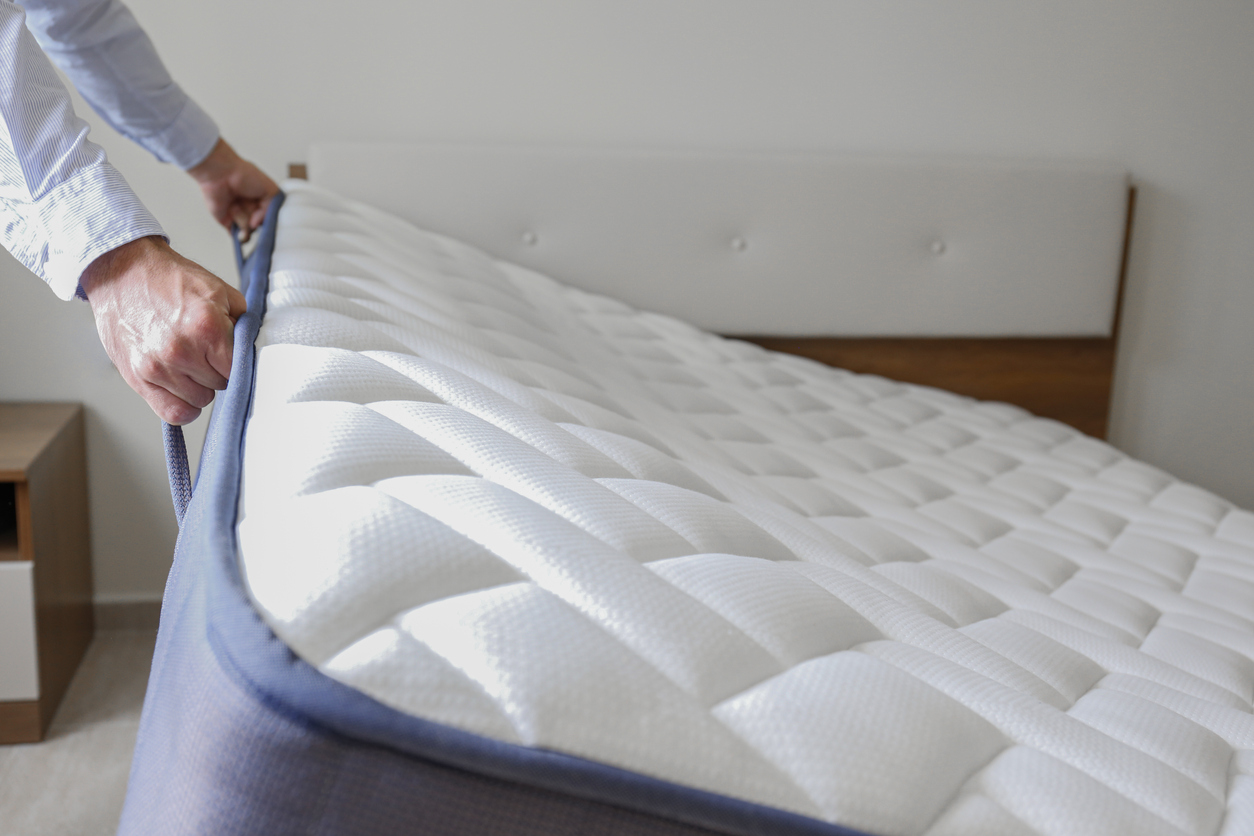 A person lifts a mattress in good condition from a small bedframe.