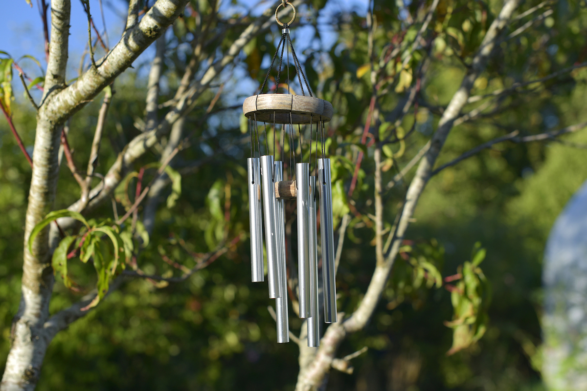 Silver wind chimes are hanging from a tree.