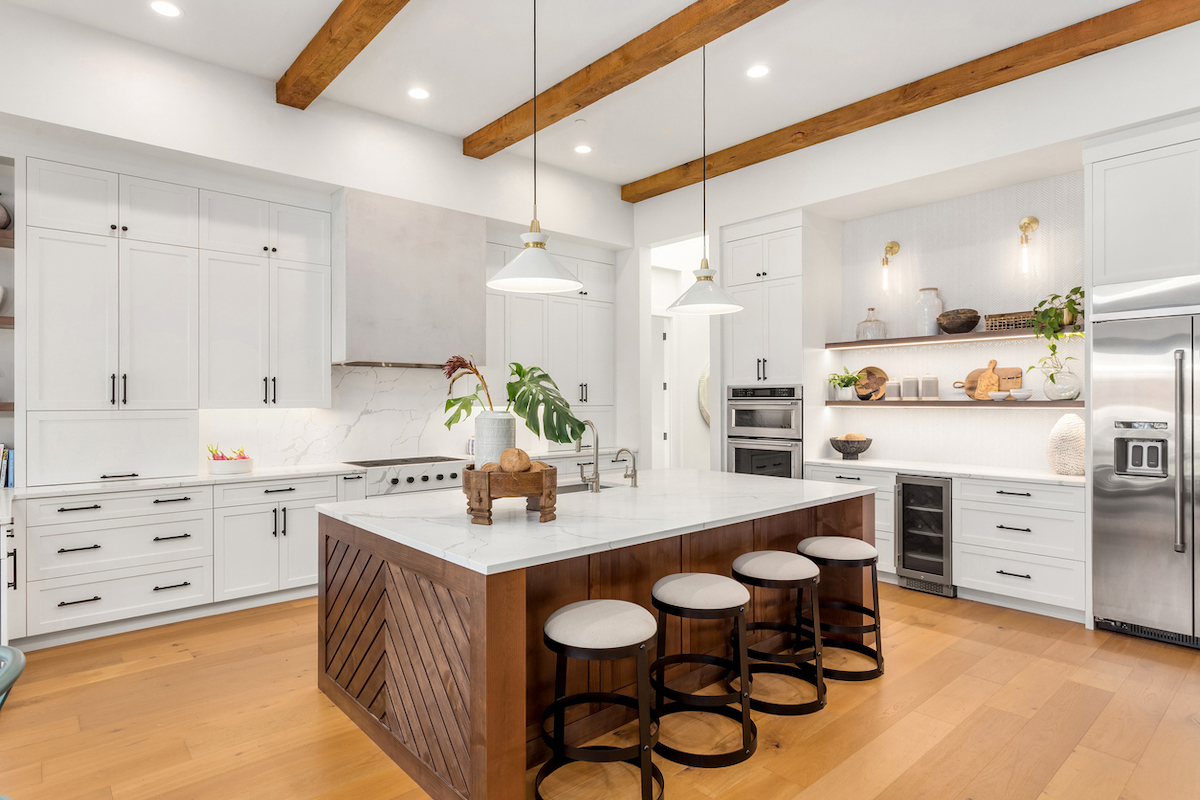 A modern kitchen features hard flooring, stainless steel appliances, and a kitchen island with a white countertop and wood design.