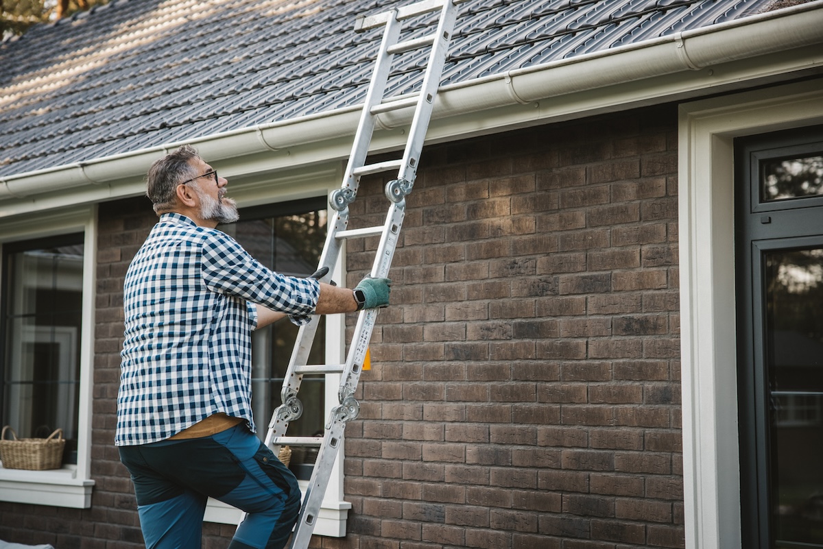 A person climbing a ladder to reach the gutters on a home.