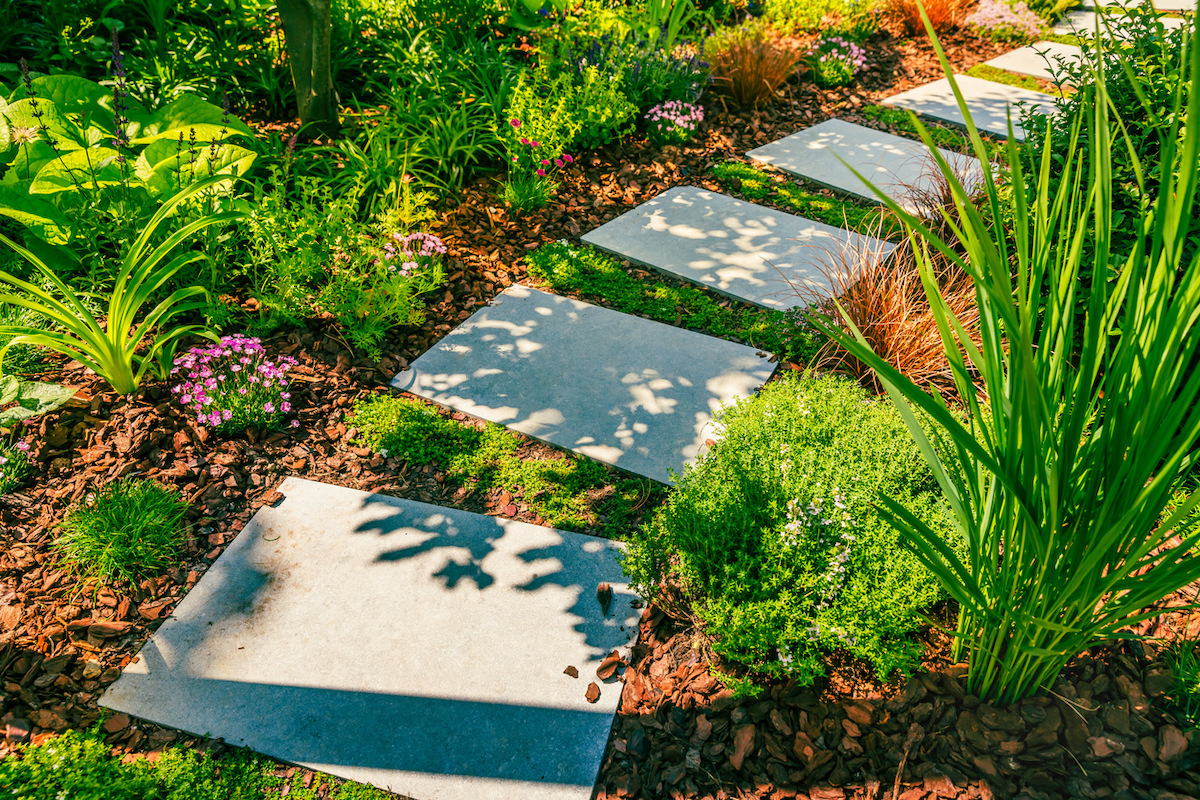 A stone garden pathway is within mulch and native grasses.