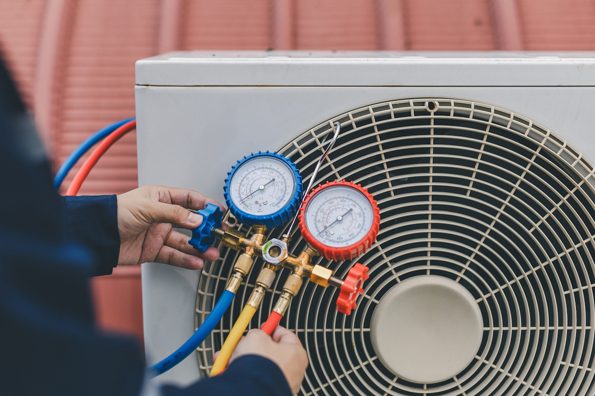 An HVAC technician is using gauges to check an outdoor air conditioner.