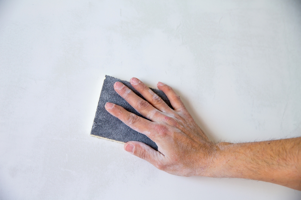 Hand is sanding wall with sanding block.