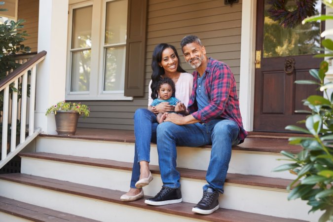 A couple with their baby are sitting on their porch steps.