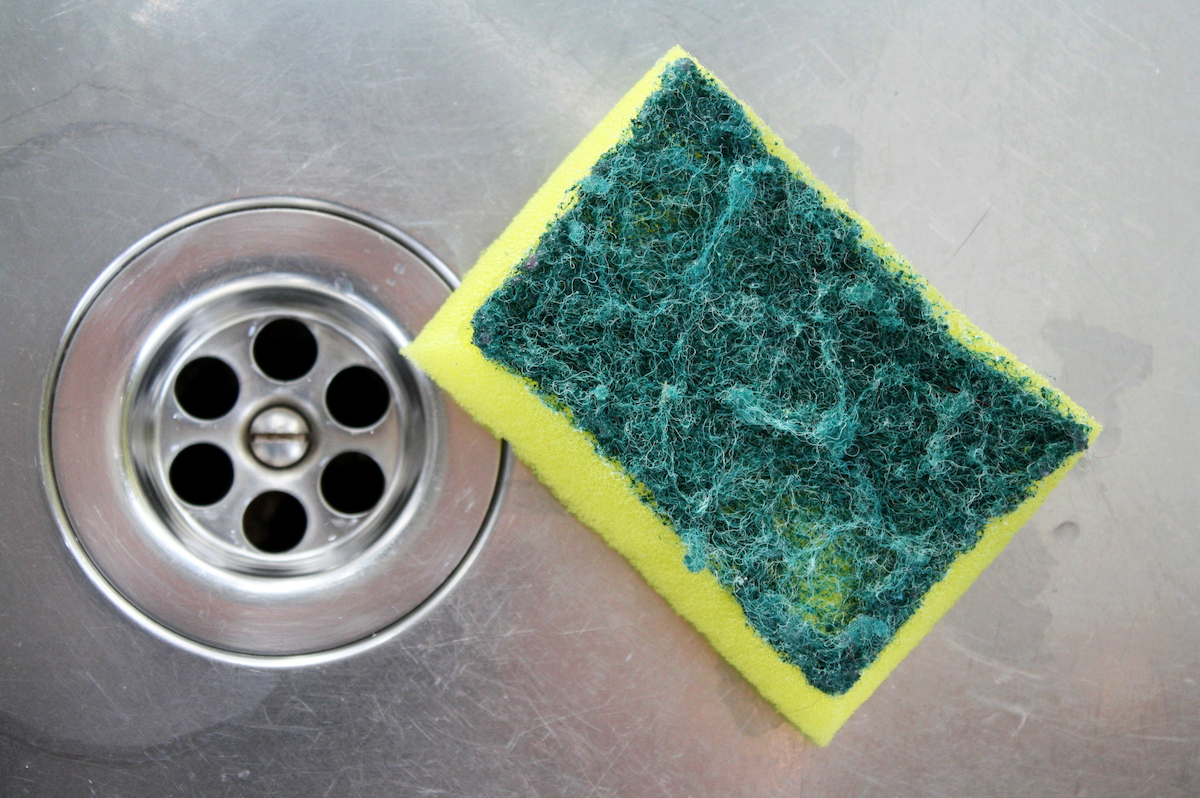 Yellow and green kitchen scrub sponge in a stainless sink. 