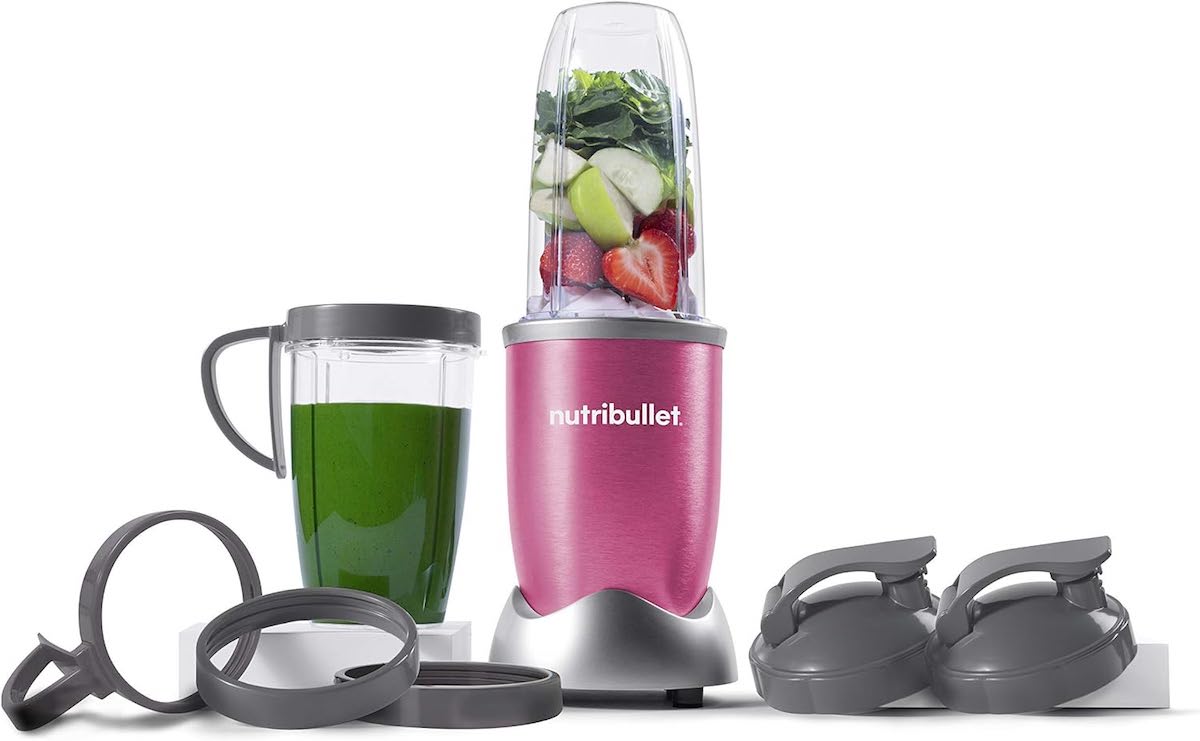 A berry pink nutribullet Pro 900 Watt blender sits next to a green smoothie and various lids.
