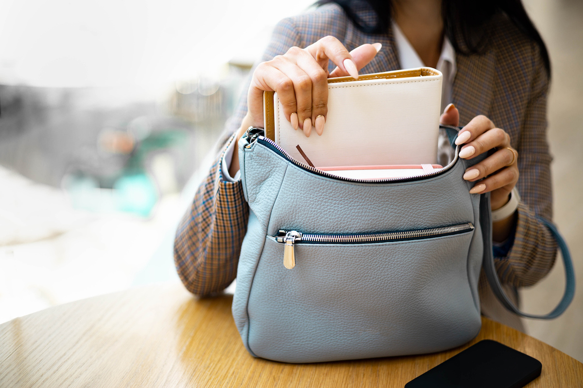Woman grabs a notebook out of a light blue purse resting on a table.