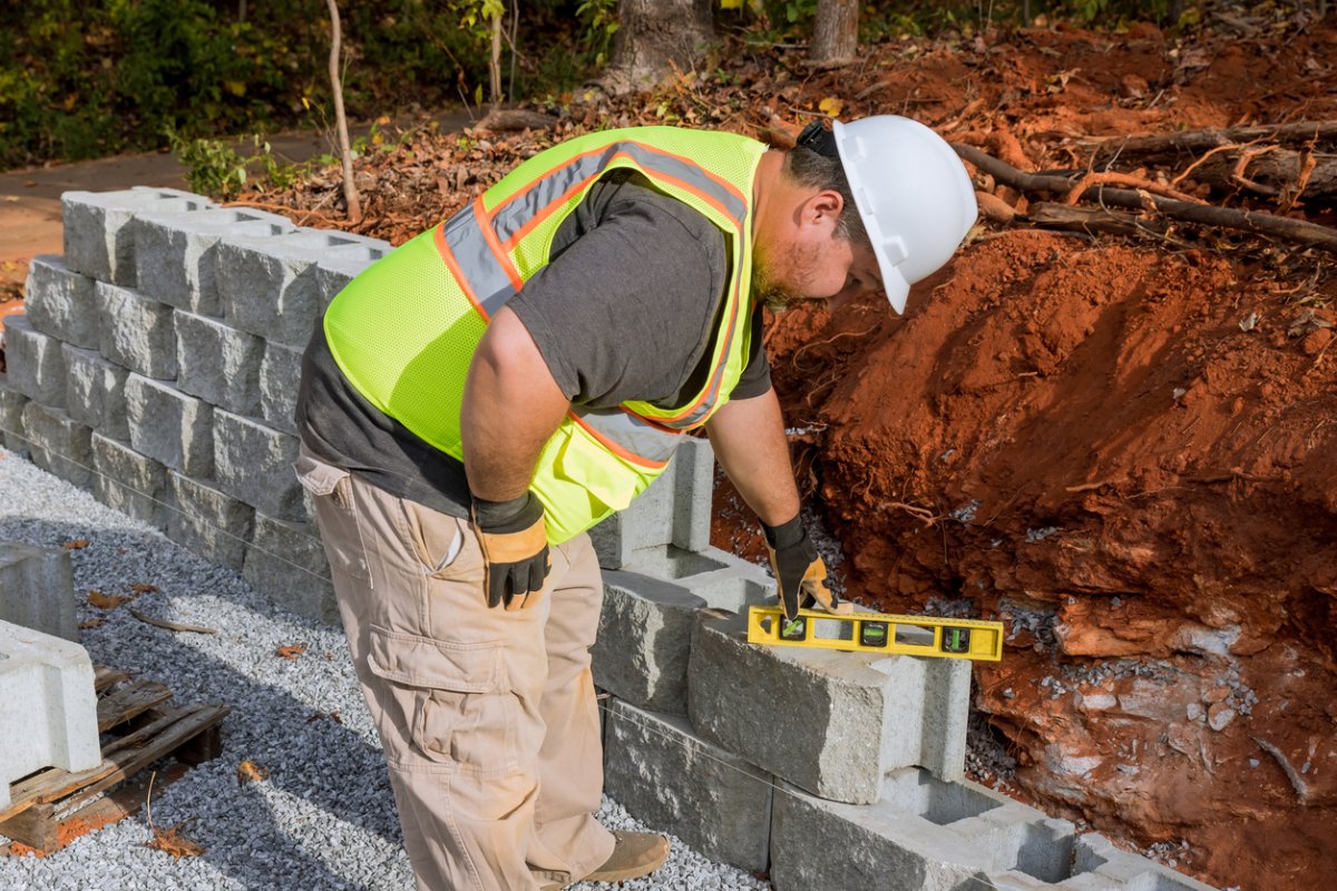 A railroad tie retaining wall under construction with a worker using a tool.