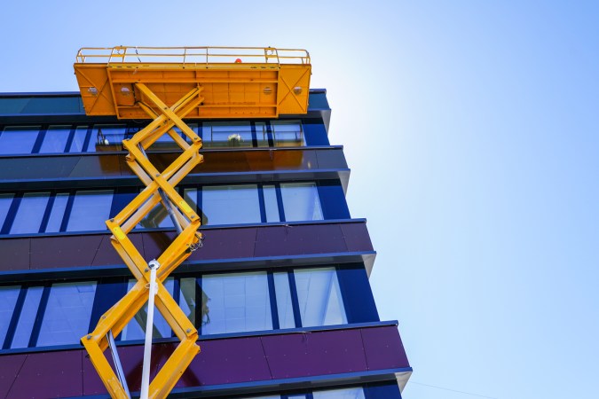 A view of a yellow scissor lift next to a building.