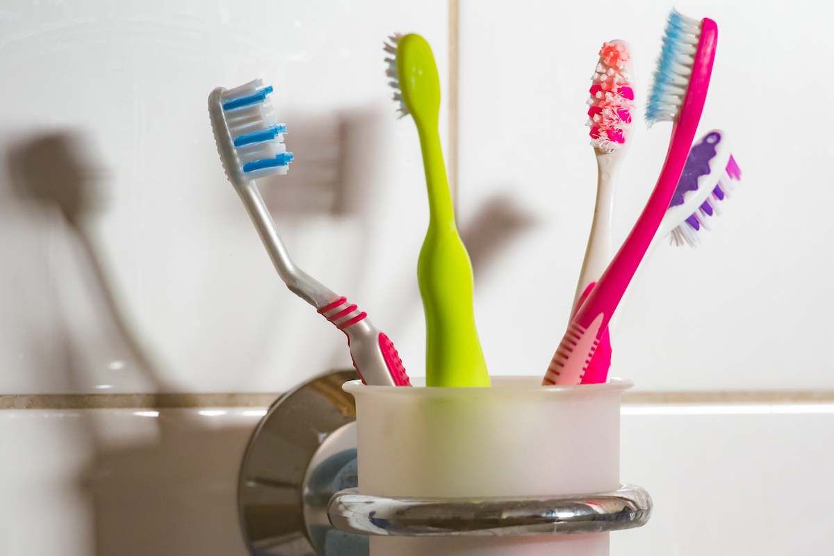 Five colorful toothbrushes are held in a toothbrush cup in the bathroom.