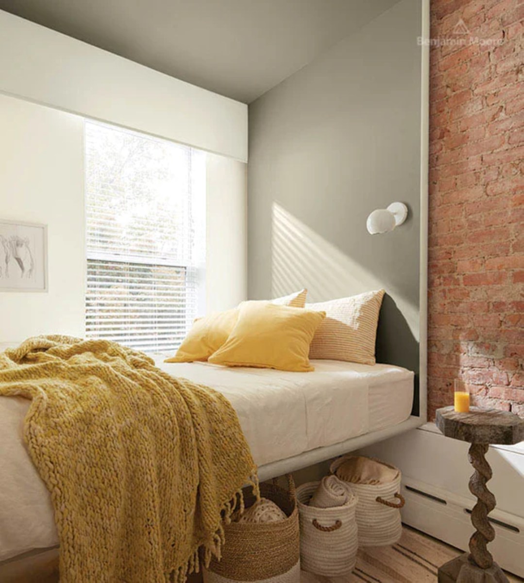A small bedroom with dark sage ceiling and a brick wall.