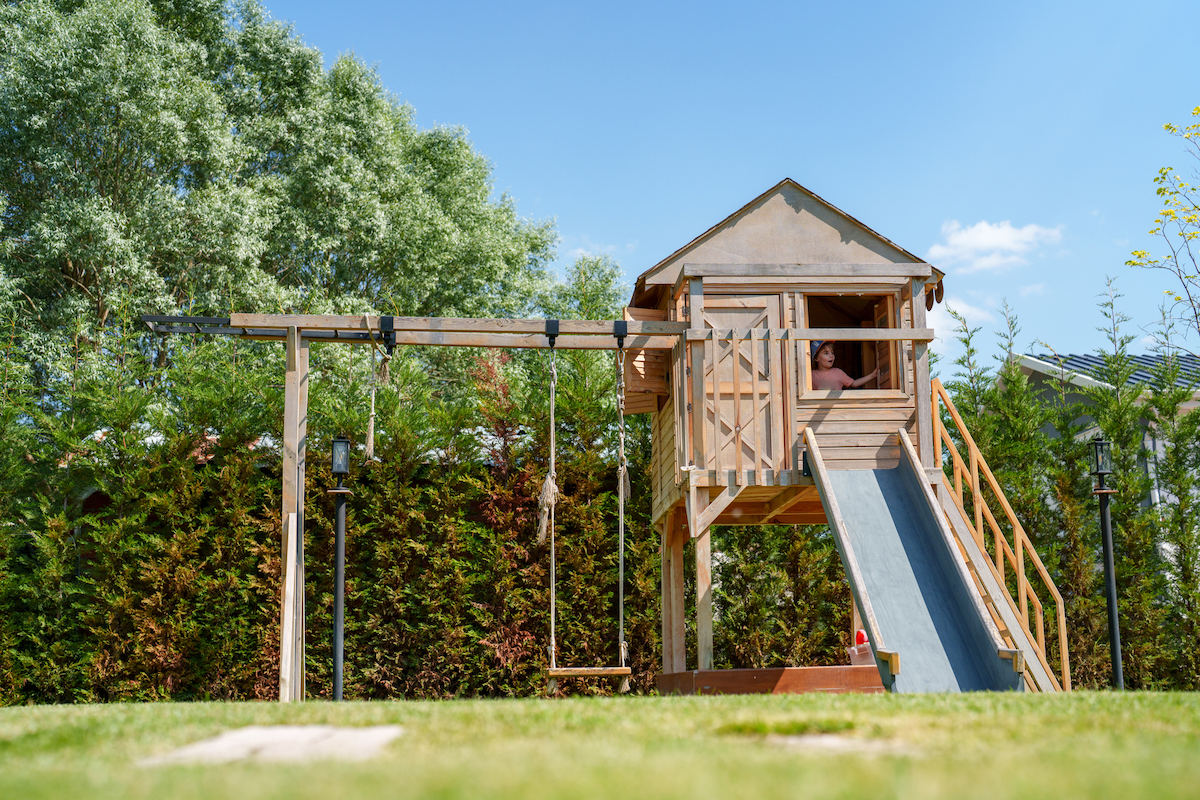 Wood backyard swingset with clubhouse and a slide.