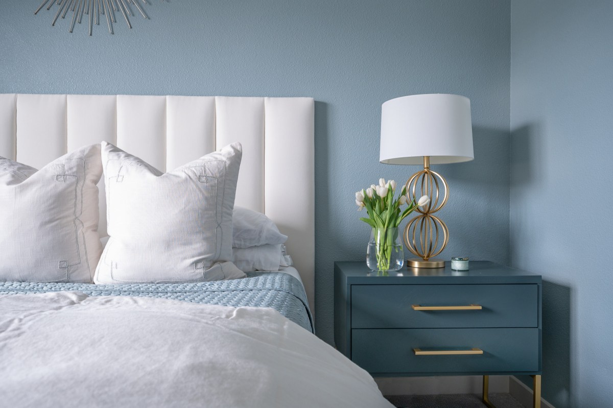 A white bed and blue nightstand sit against a blue painted wall.