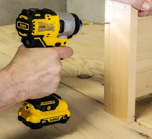 Person using a DeWalt impact drill to screw a nail into wood
