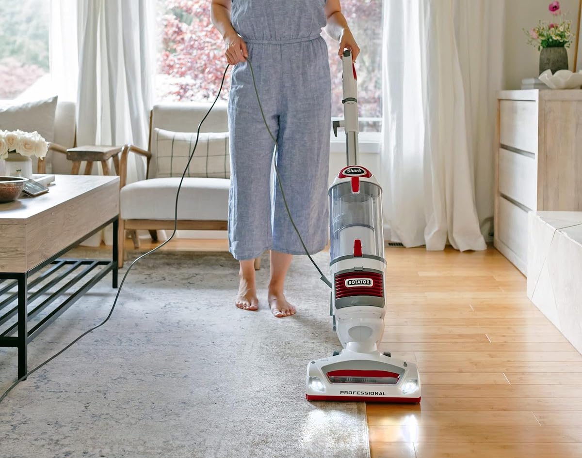 A woman is using a Shark Rotator Professional Lift-Away Upright Vacuum to vacuum a rug on a hardwood floor.