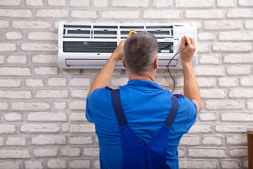 A worker fixes an AC mounted on a white brick wall.