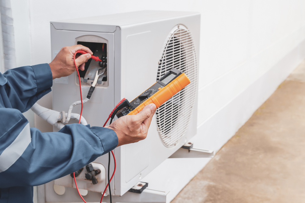 A close up of a worker using a multimeter to test an AC unit. 