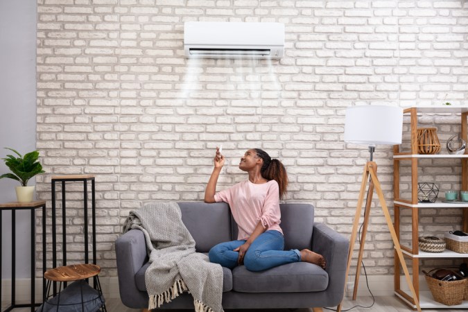 A woman sits under an AC mounted on a white brick wall.