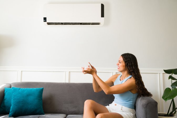 A woman sits on a couch below an AC unit.