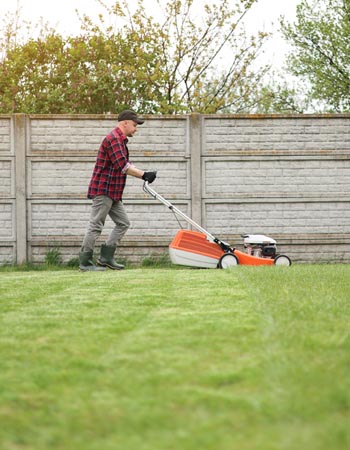 A man in flannel mows a lawn. 