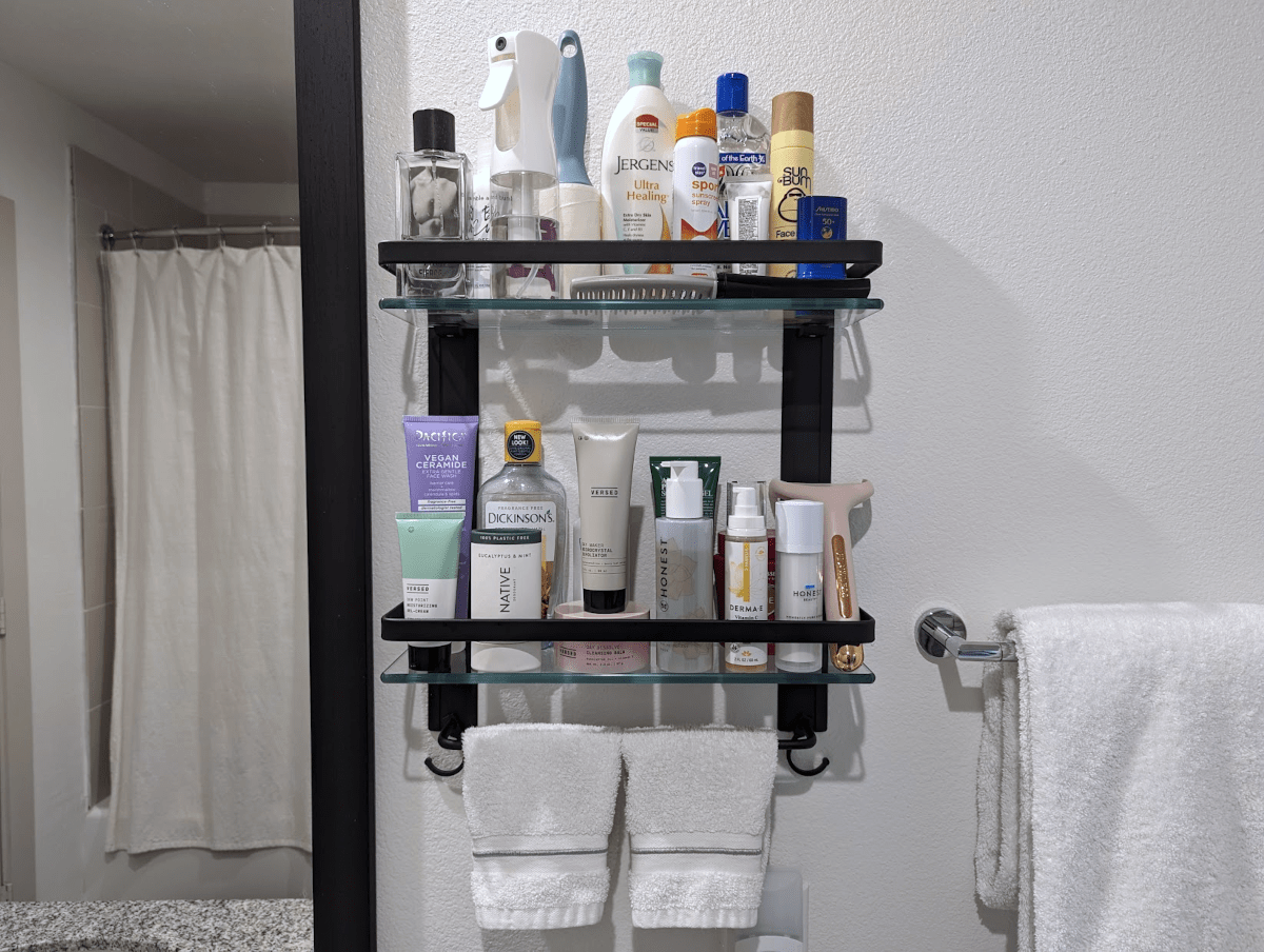 A mounted black metal and clear glass shelf next to a bathroom mirror.