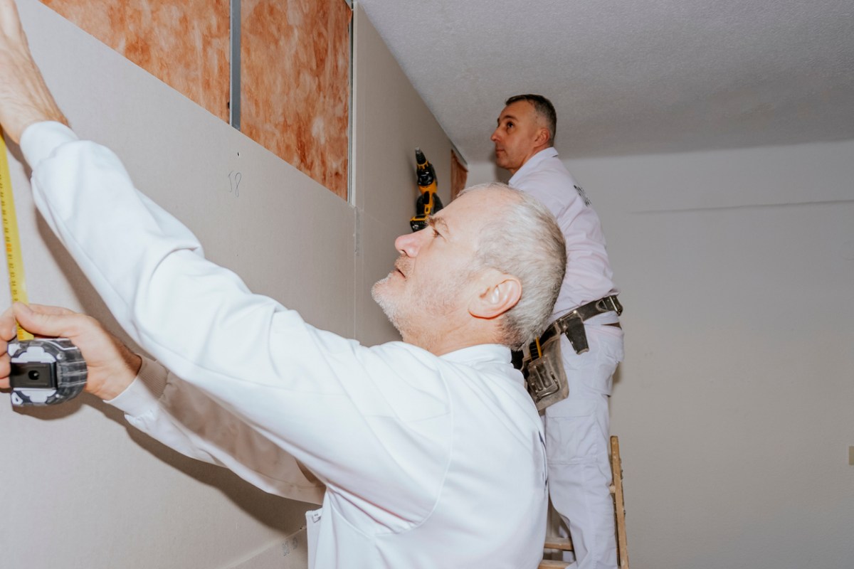 Two men measuring drywall in a room