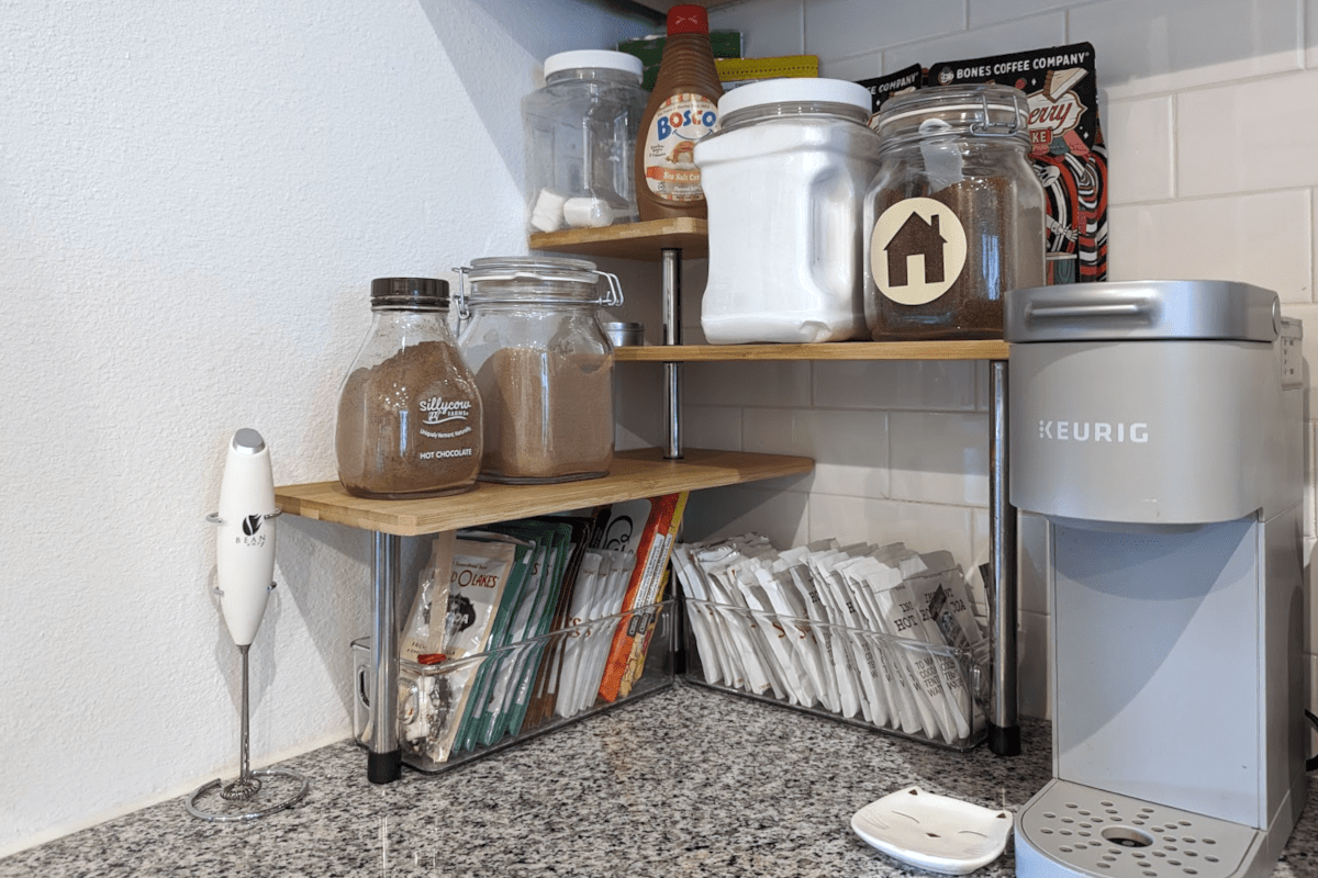 A three-tiered bamboo shelf organizer in the corner of a kitchen countertop.