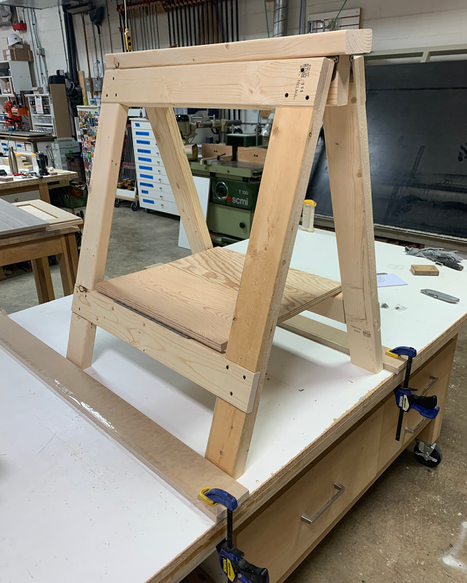 A DIY sawhorse braced on a workbench in order to secure the folding shelf in between the legs.