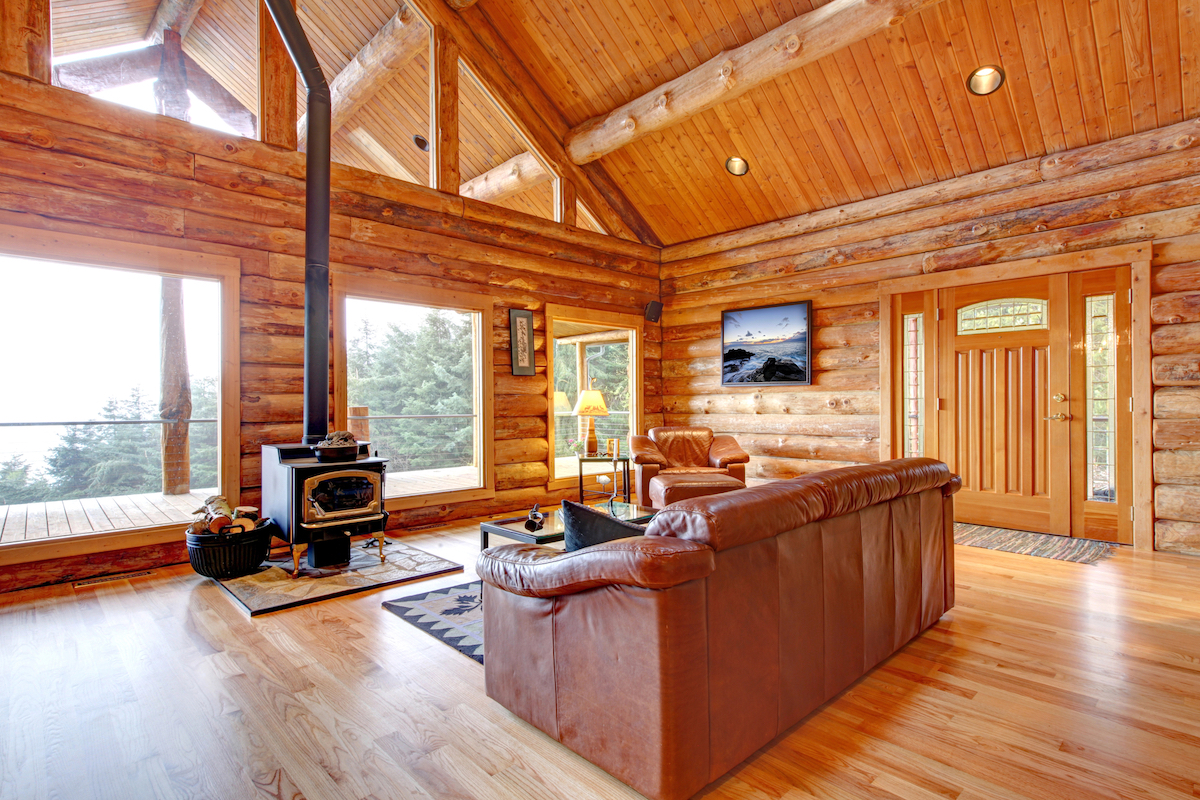 The interior of a luxury log cabin living room includes hardwood flooring, a leather couch, and a small wood stove.