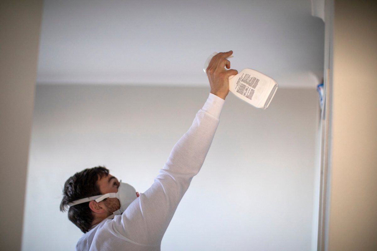 A person spray a solution on a wall while wearing a protective mask.