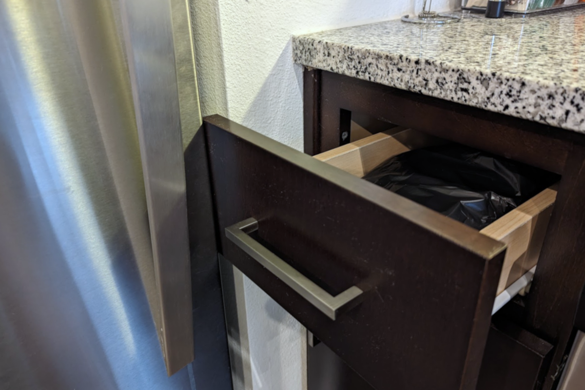 A small kitchen drawer partially open, its face touching a stainless steel refrigerator.