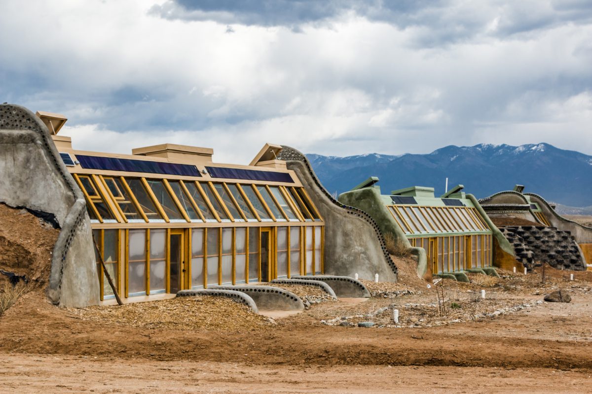 A row of three earthship homes sit side-by-side in the New Mexico desert landscape.