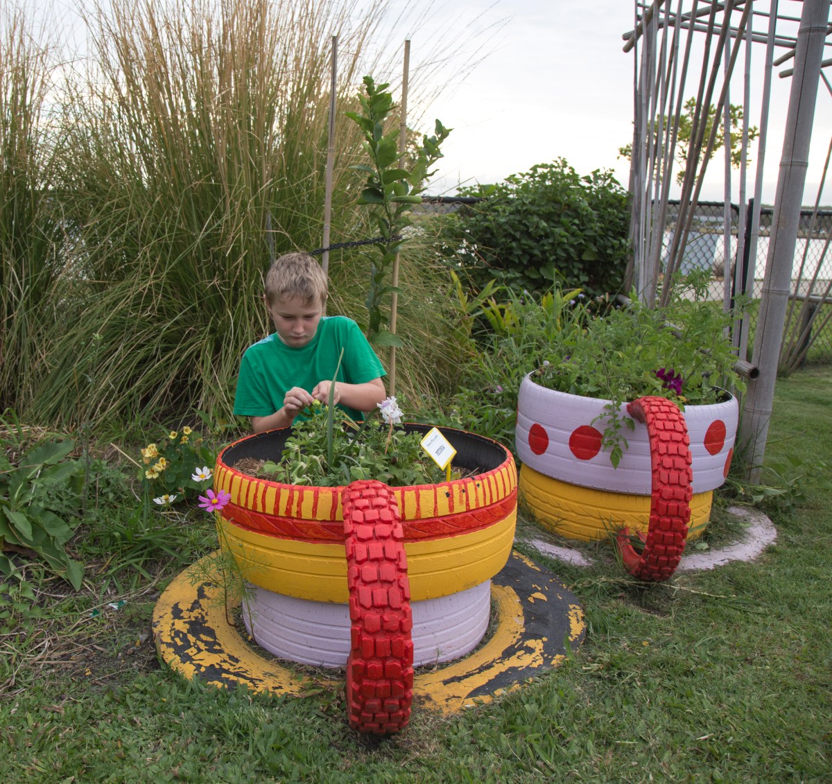 A kid works with plants in a planter made of painted tires.