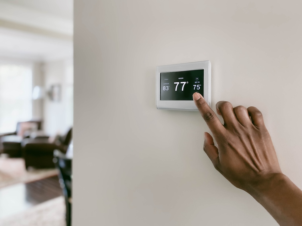 A person adjusting their thermostat during the dog days of summer to save energy and money.