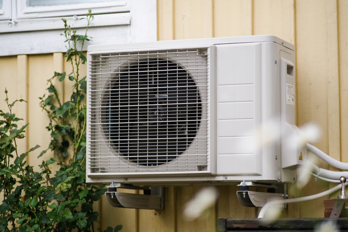 A heat pump unit installed on side of a yellow exterior wall.