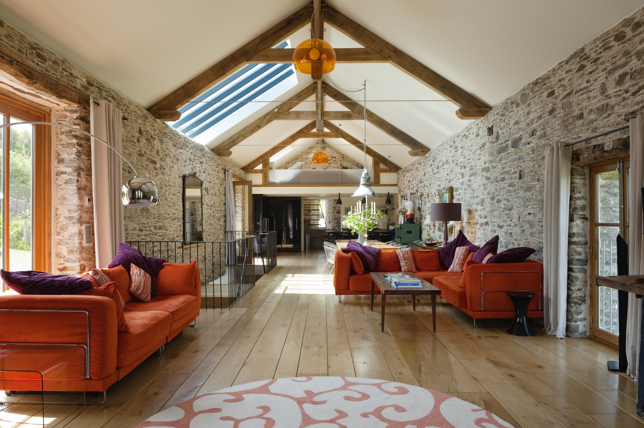 The long interior of a home converted from a European barn is finished with hardwood and furnished with red sofas.
