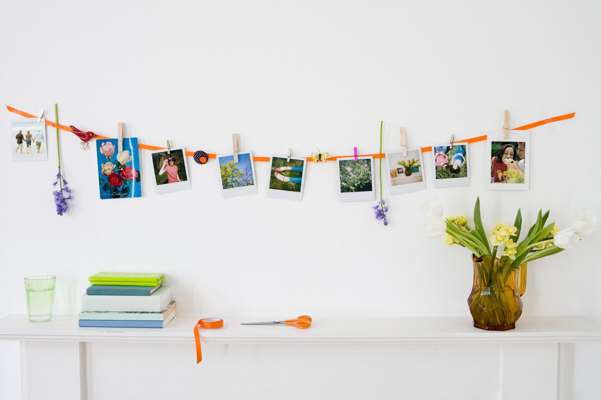 Clothes pins hold photos along a garland on a white wall.