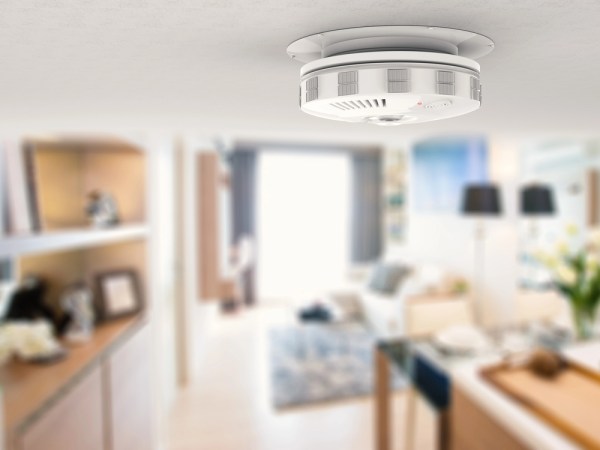 A close up of a smoke alarm against the a blurred background picturing a living room.