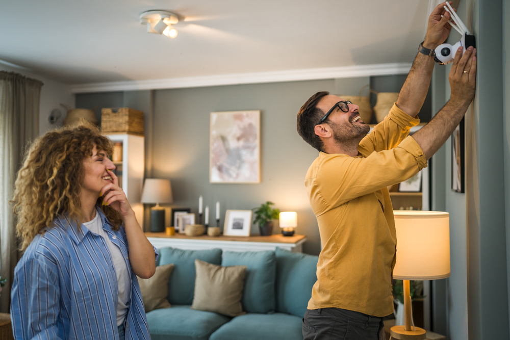 A man and a woman set up a home security system in a living room.