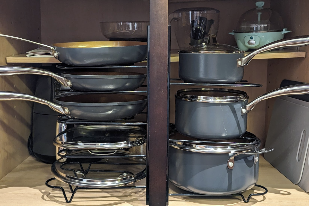 A Gotham ceramic cookware set stacked onto a wire organizer inside of a kitchen cabinet.