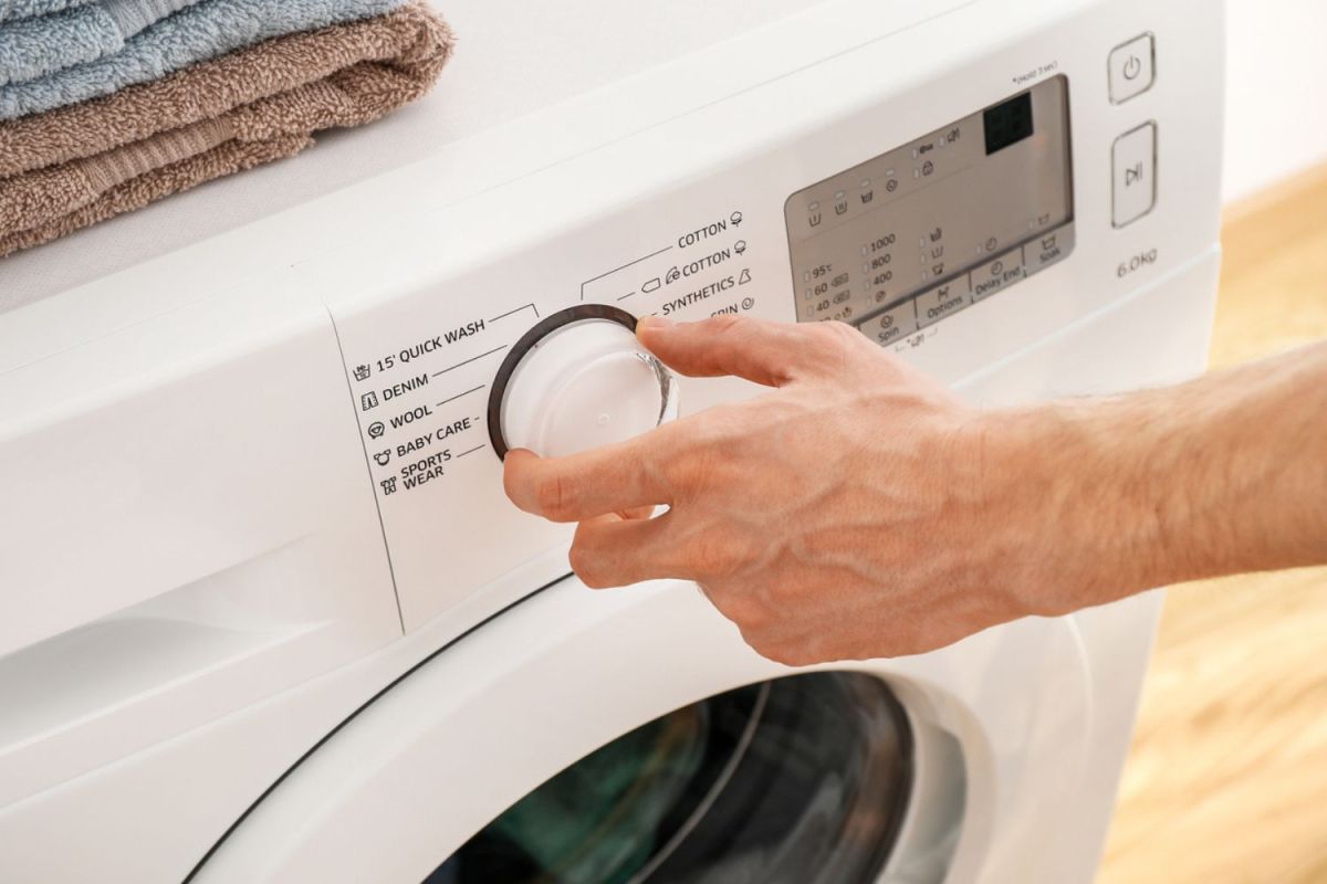 A close up of a person turning the knob of a washing machine. 